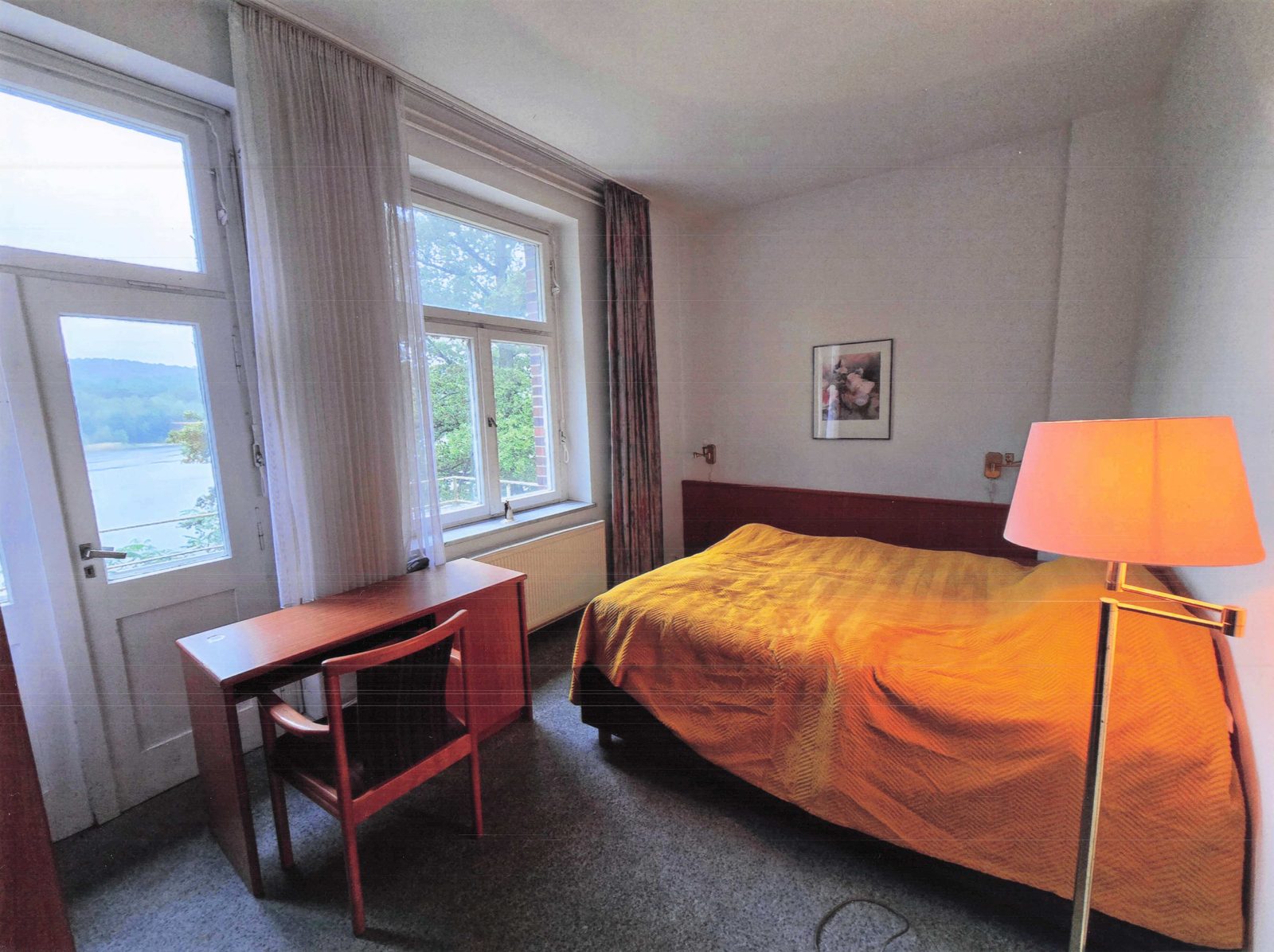 Hotelzimmer mit orangefarbenem Bettüberwurf und Seefenster II